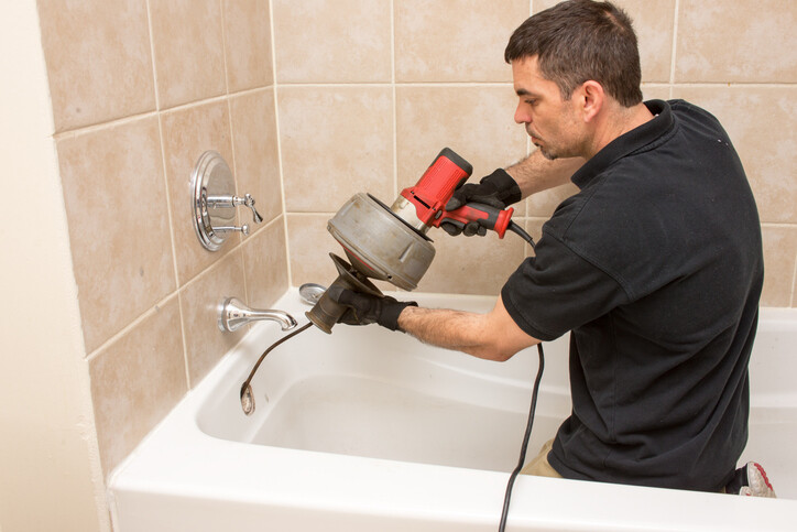 Man using drain snake to clean bath drain