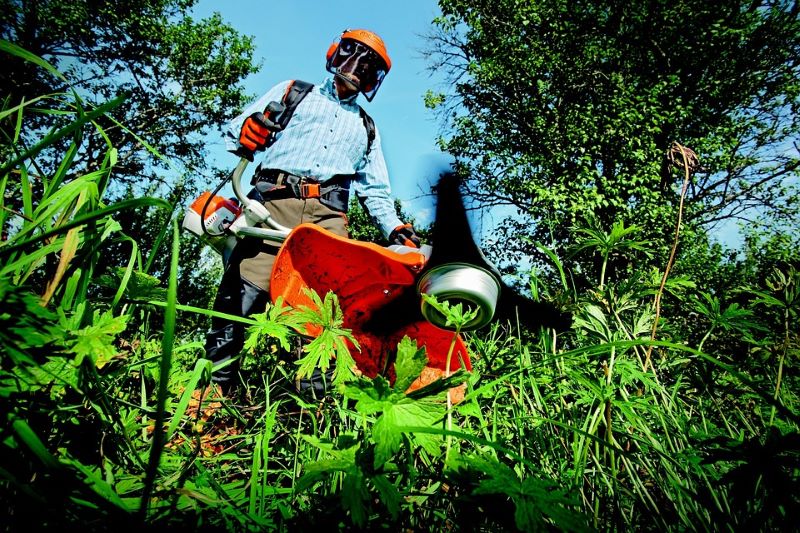 man-wearing-protective-face-screen-using-garden-strimmer