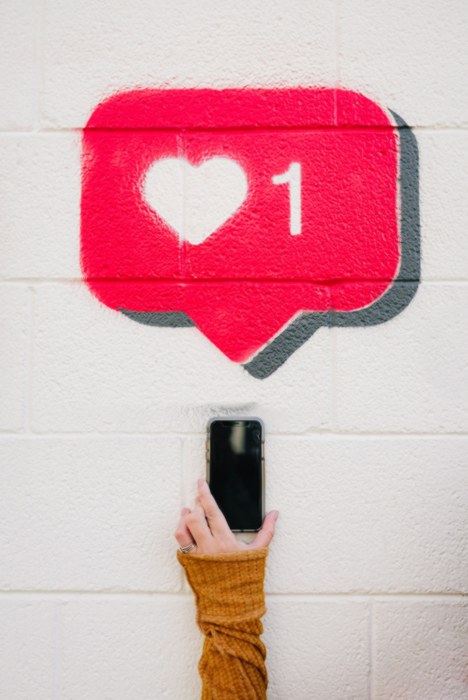 Outstreched arm with phone sliding towards graffitti on white wall of red comment box containing a white heart and a number 1.