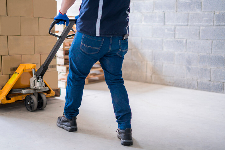 worker dragging pallet truck loaded with boxes